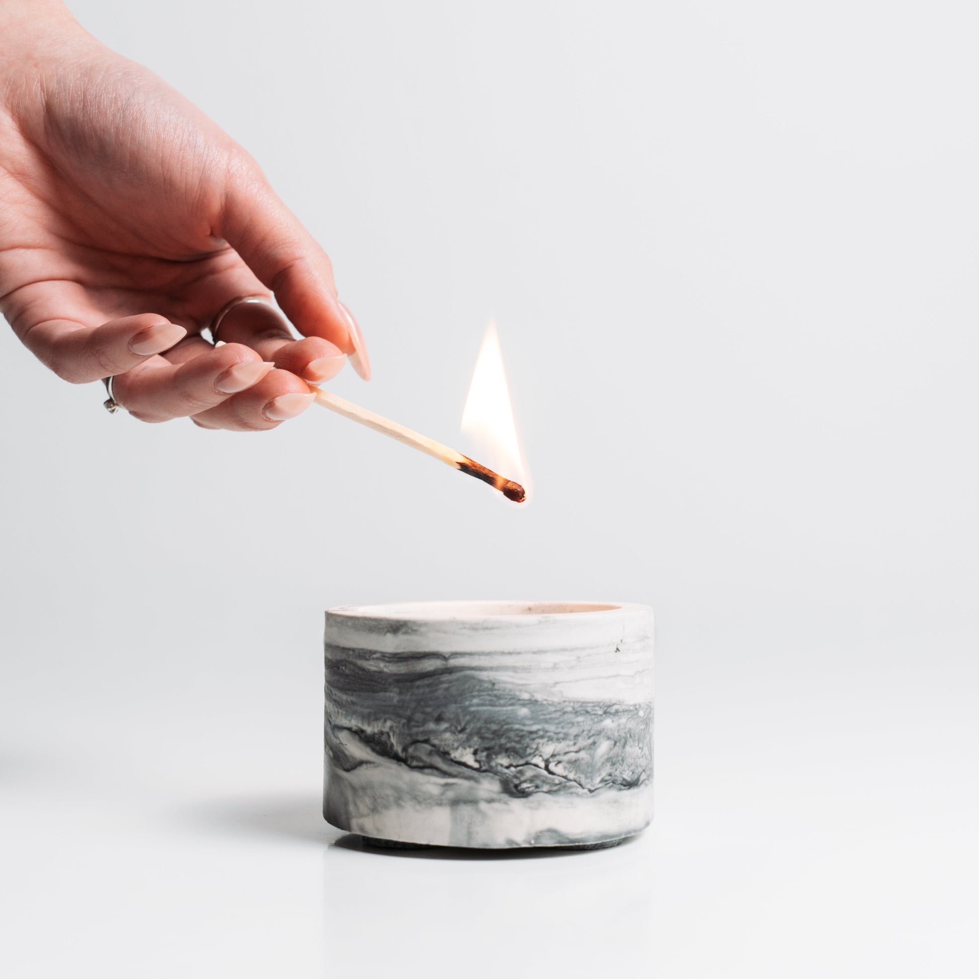 Hand lighting a candle with a match on a light gray background